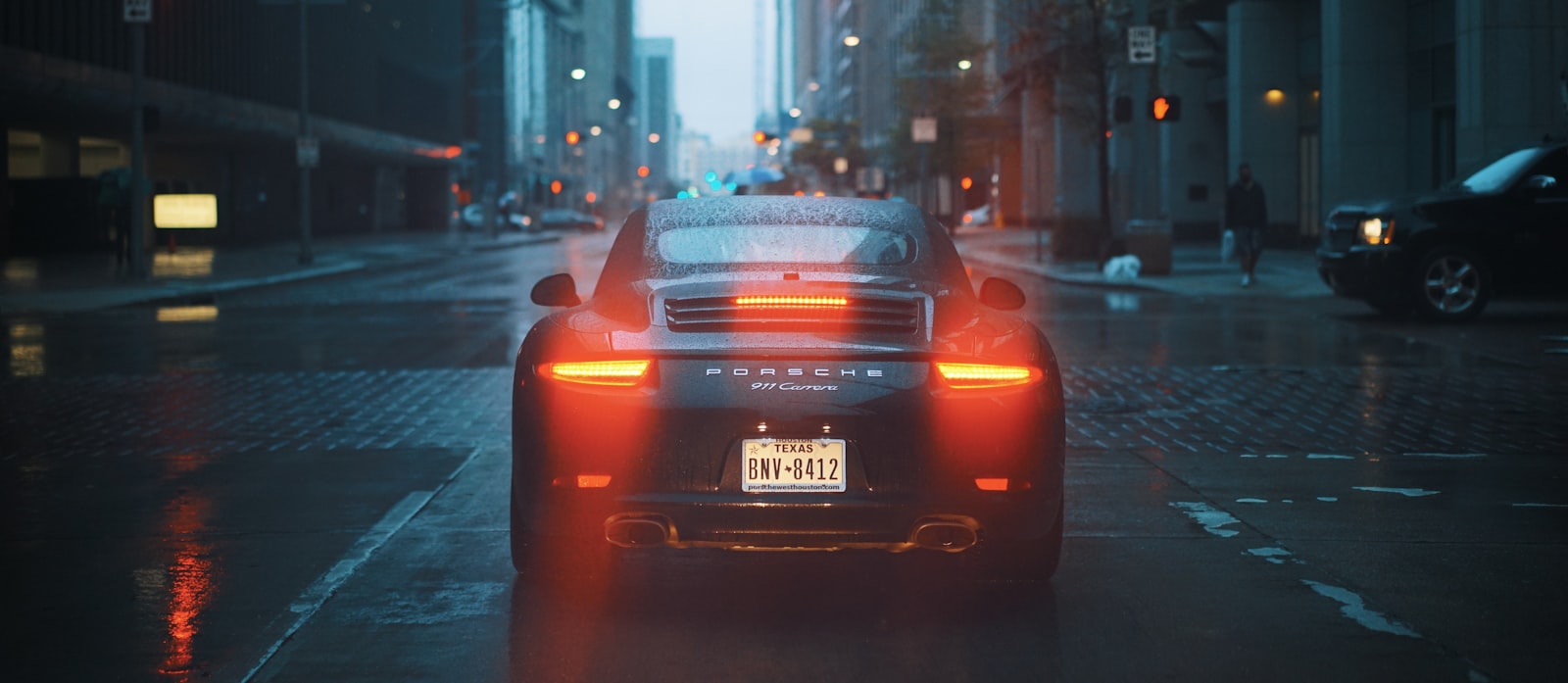 Tail lights of a car in a rain-soaked city at dusk