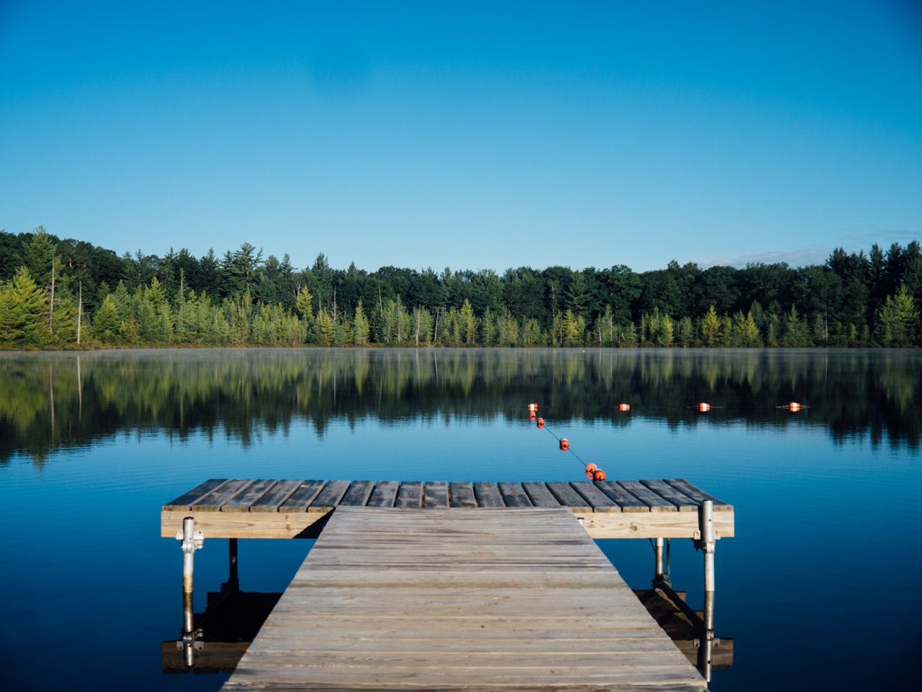 A wooden dock reaching into a perfectly still lake