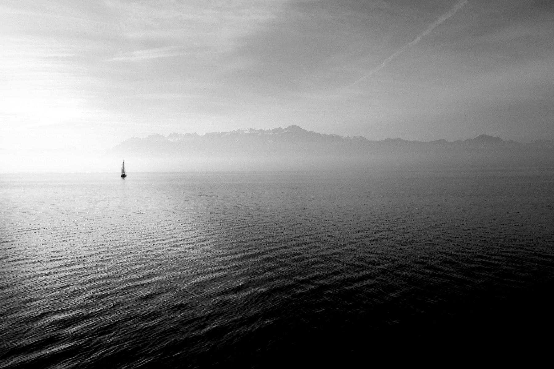 A lone sailboat on a still, misted sea