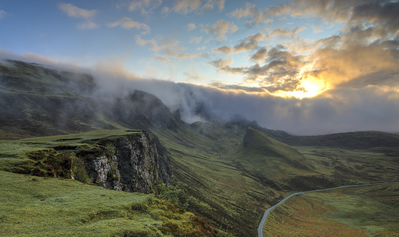 A narrow road winding through green highlands under morning fog
