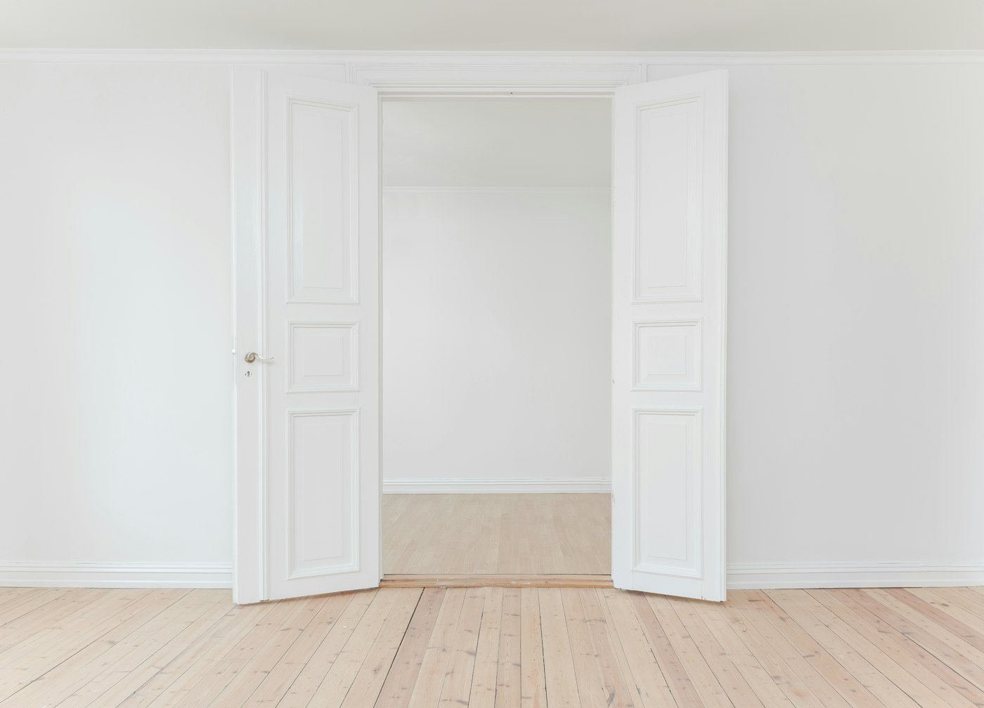Tall white double doors opening into a bright, empty room